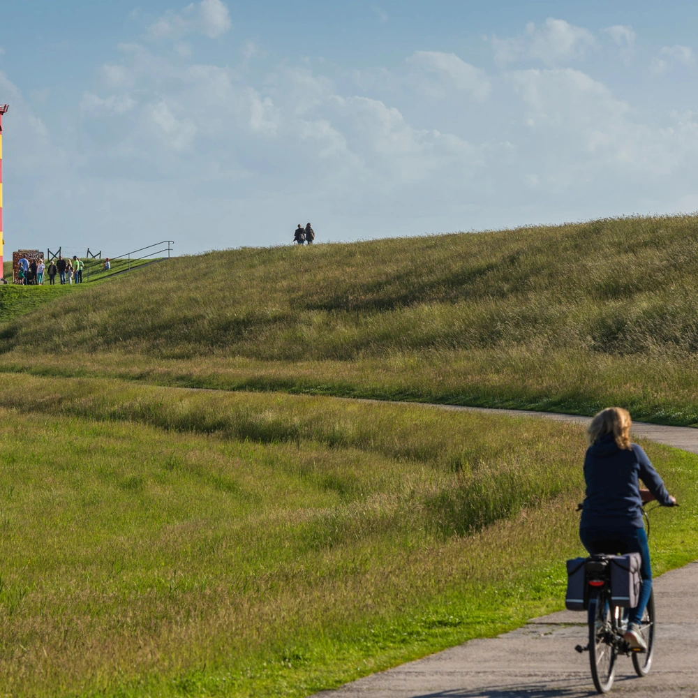 Entdecke die schönsten Radtouren in Niedersachsen Frau fährt mit einem Fahrrad zum Pilsumer Leuchtturm in Ostfriesland