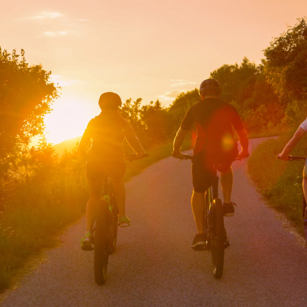 Entdecke den E-Bike Hersteller Riese & Müller Drei Personen fahren mit E-Bikes im Sonnenuntergang