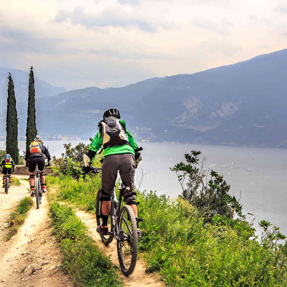 Dieses Jahr feiert das Riva del Garda Bike Festival 30-jähriges Jubiläum. Familie fährt bergige Straße neben Gardasee entlang.