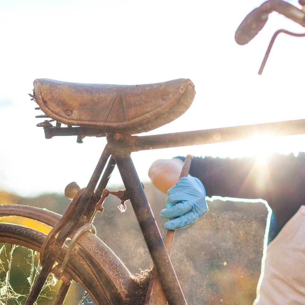 Frau reinigt ein altes Fahrrad im Sonnenlicht mit blauen Handschuhen.