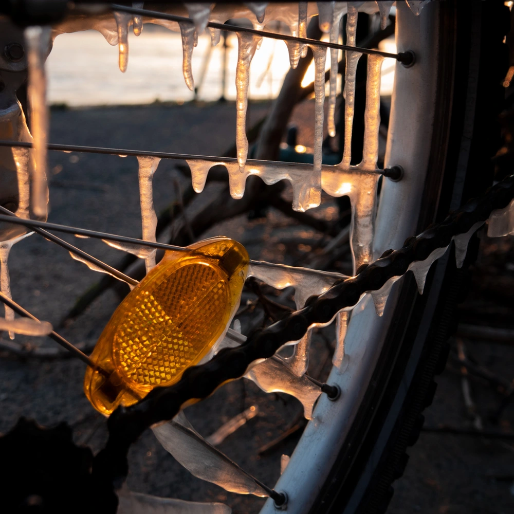 Detailaufnahme eines Fahrradkettenantriebs mit Eis und Sonnenlicht im Hintergrund.