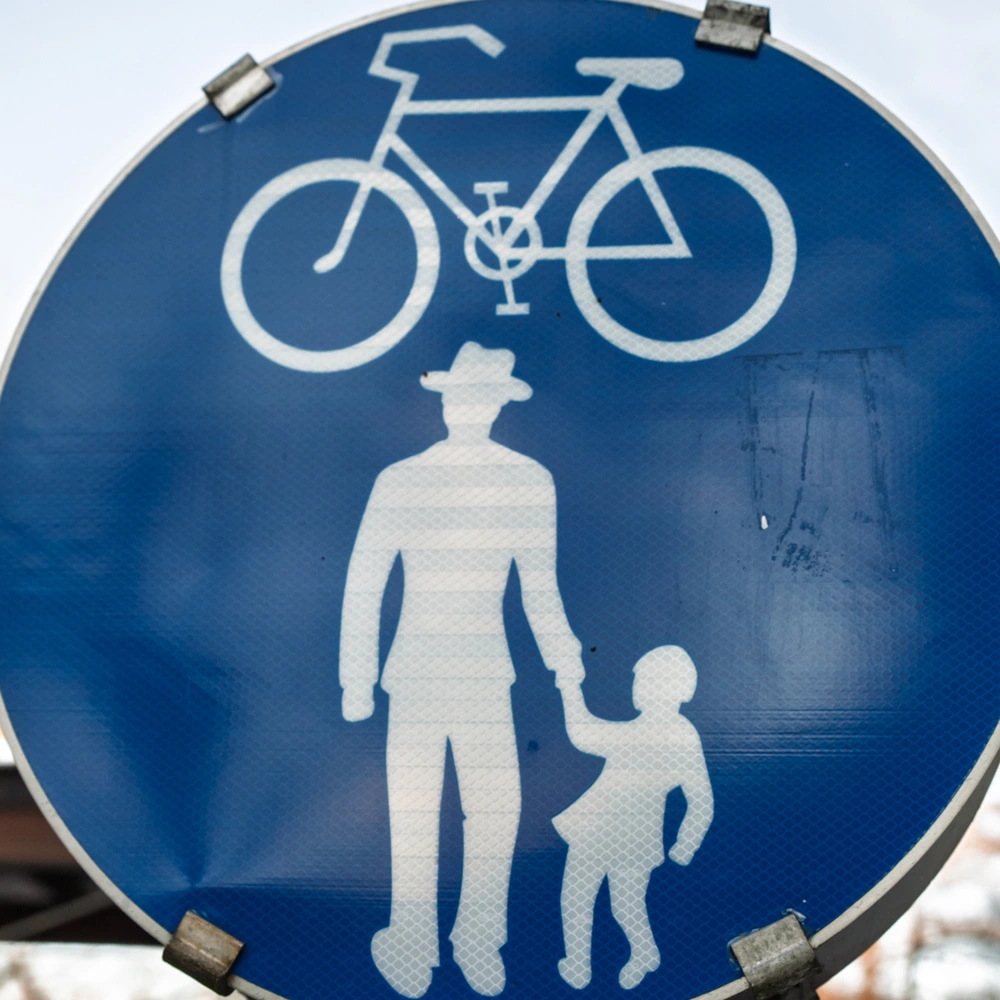 Blaues Straßenschild mit einem weißen Fahrrad und einem Erwachsenem mit Kind