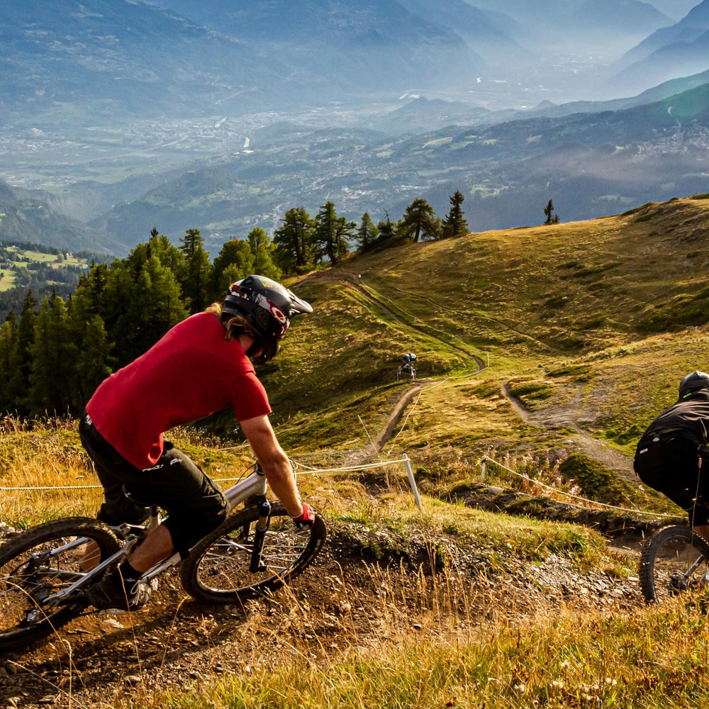 Zwei Mountainbiker fahren die hügelige Strecke in malerischer Berglandschaft.