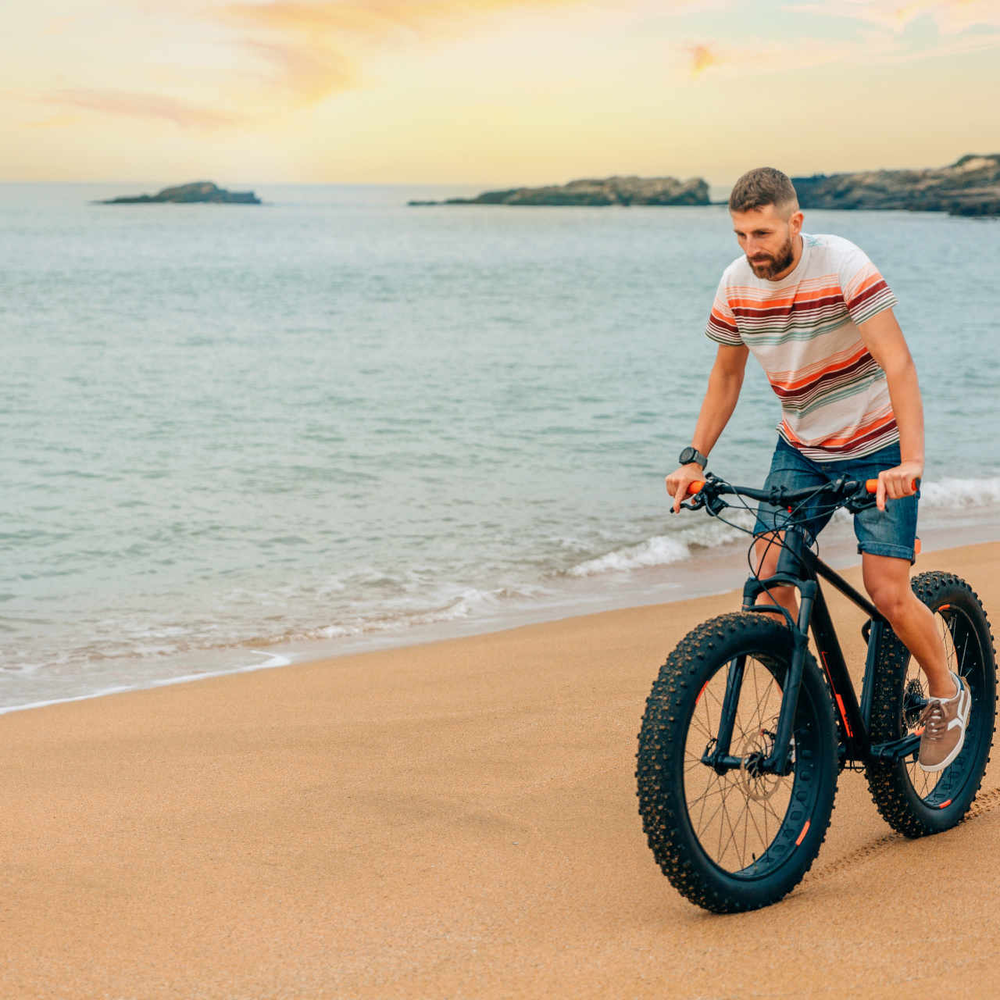 So bauen Sie Ihr Fatbike ganz einfach auf Tubeless-Reifen um. Mann fährt auf Fatbike Strand entlang.