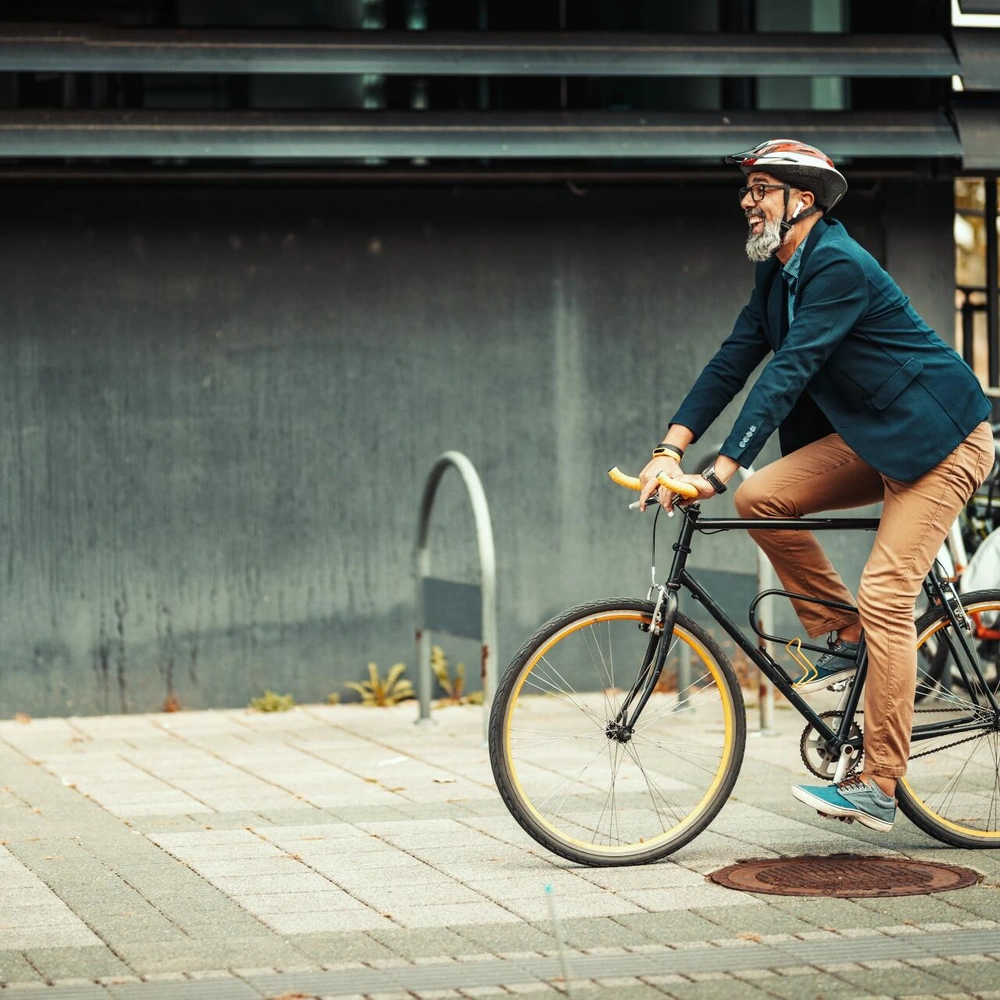 Alterer Mann im Sakko fährt fröhlich mit einem urban Bike auf einem Gehweg.