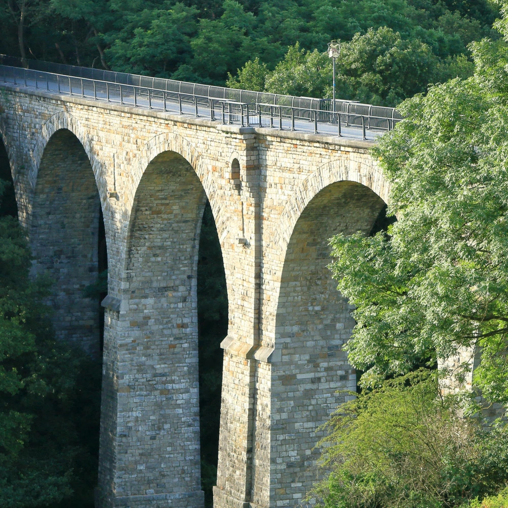 Viadukt der Vennbahn zwischen Aachen Brandt und Kornelimünster Steinernes Viadukt mit mehreren Bögen, umgeben von Bäumen und Grün.