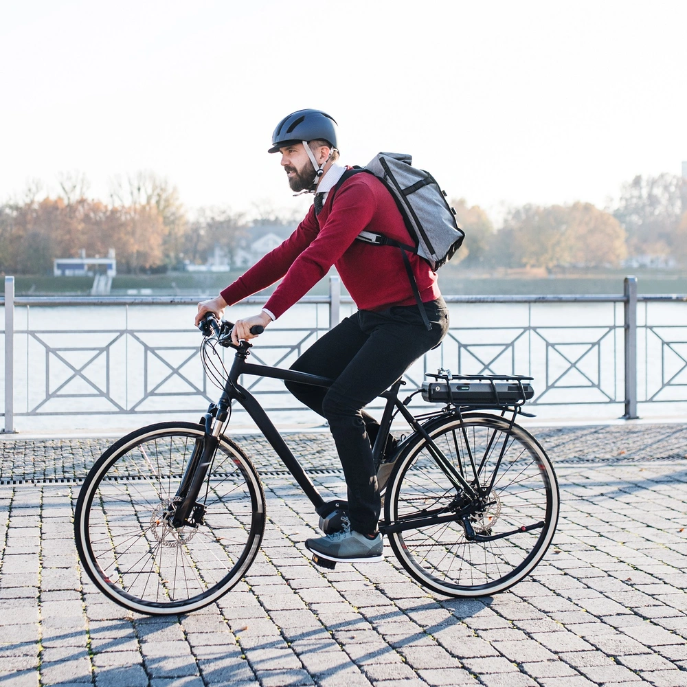 Vergleichstest Fahrradrucksäcke Radfahrer mit Rucksack fährt in städischer Kulisse neben einem Fluss.