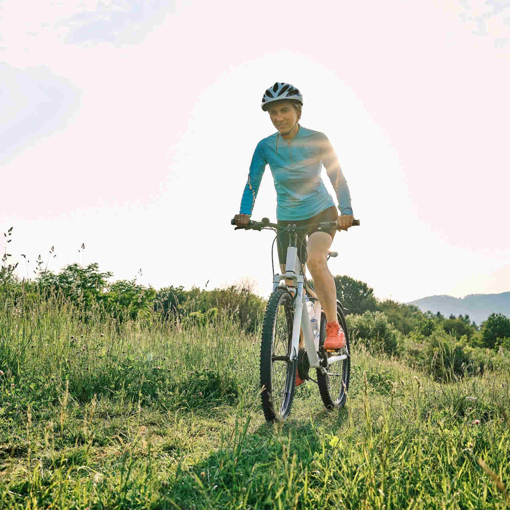 Waldbike baut umweltfreundliche Elektrofahrräder. Frau fährt mit Mountainbike über Wiese.