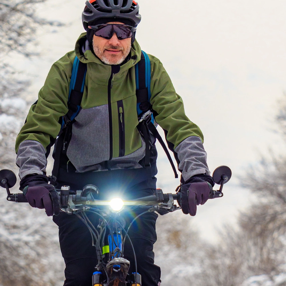 Person auf einem Fahrrad in verschneiter Landschaft, trägt Winterkleidung und Helm.