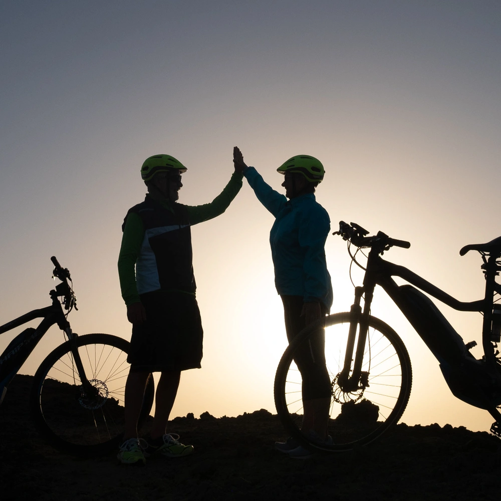 Worauf achten beim E-Bike Kauf – die wichtigsten Tipps für den perfekten Einstieg Zwei Personen stehen neben ihren E-Bikes vor dem Sonnenuntergang und klatschen sich ab