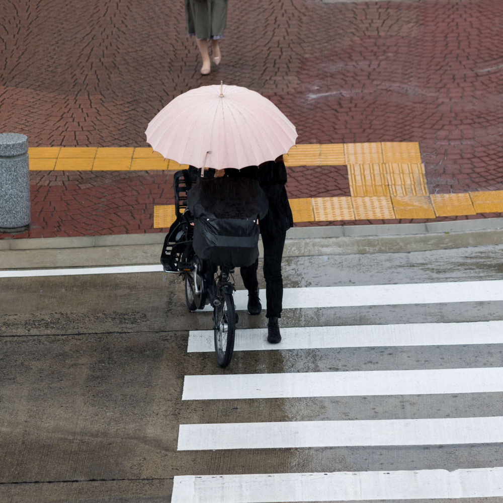 E-Bike im Regen fahren Person schiebt Fahrrad bei Regen über einen Zebrastreifen