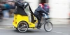 Rikscha-Fahrten für Seniorinnen Radfahrer mit einem gelben Rikschawagen fährt an einer Menschenmenge vorbei