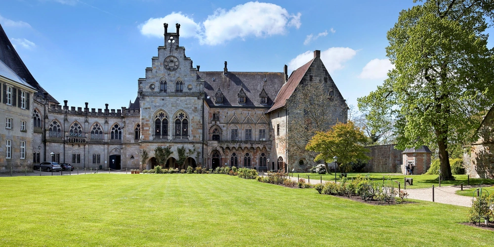 Historisches Gebäude mit Garten unter blauem Himmel und grünen Bäumen.