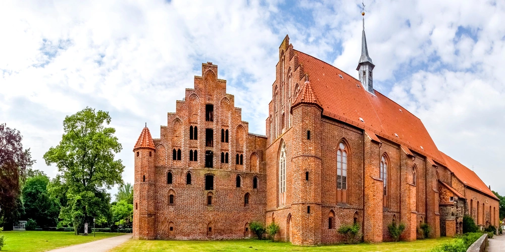 Historisches Backsteingebäude mit roten Ziegeldächern und umgebendem Grün.