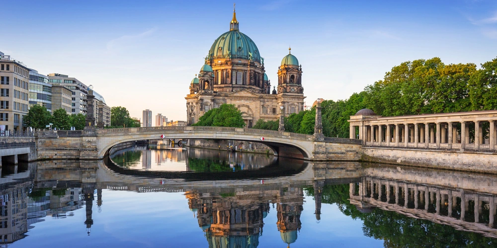 Berliner Dom mit Brücke und reflektierendem Wasser im Vordergrund.