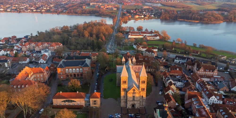 Luftaufnahme einer Stadt mit Kirche, umgeben von Wasser und Bäumen bei Sonnenuntergang.