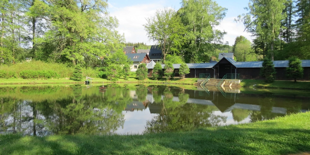 Ruhiger Teich umgeben von üppigem Grün und historischen Gebäuden.