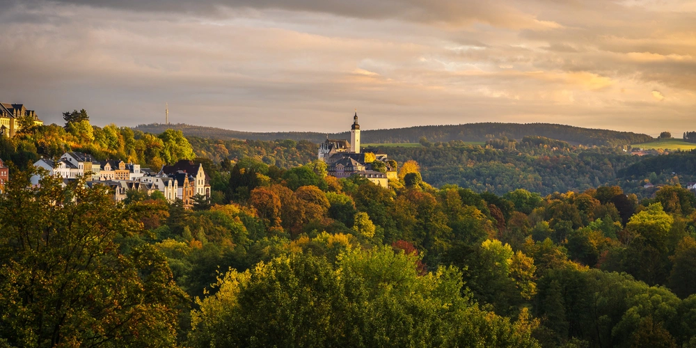 Herbstliche Landschaft mit einer Stadt und einem Kirchturm in der Ferne.