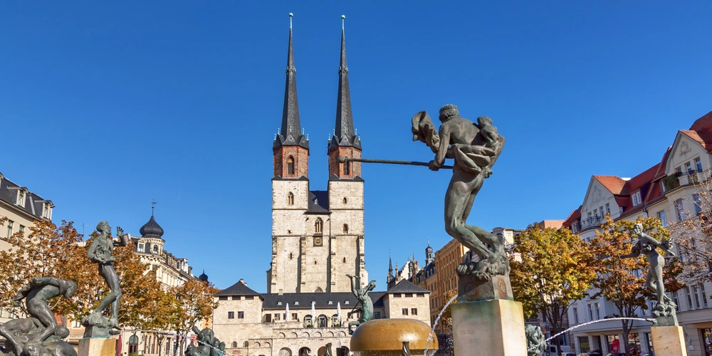 Platz mit zwei hohen Türmen und einer Skulptur von tanzenden Figuren, Herbstsonne.