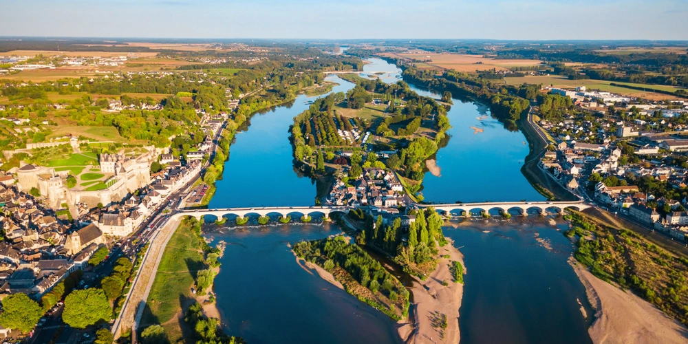 Luftaufnahme eines Flusses mit Brücke, umgeben von grünen Bäumen und Häusern.