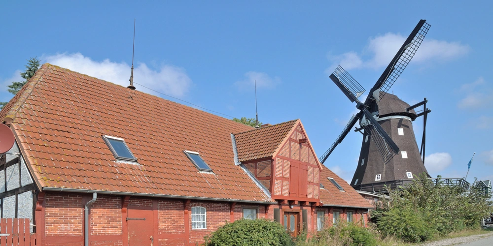 Rote Fachwerkhäuser neben einer alten Windmühle unter blauem Himmel.