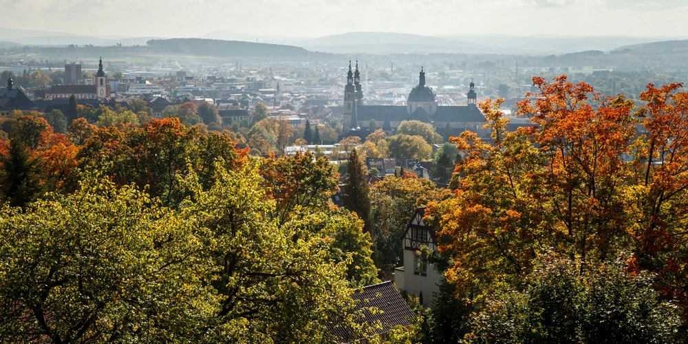 Blick über eine Stadt mit herbstlichen Bäumen und historischen Gebäuden.