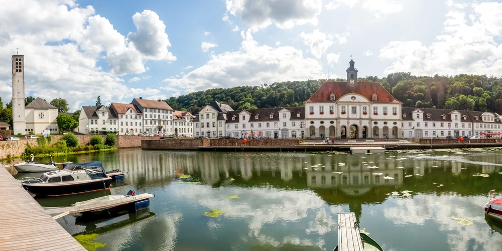 Panoramablick auf ein historisches Gebäude am Fluss mit Booten und Wolken am Himmel.