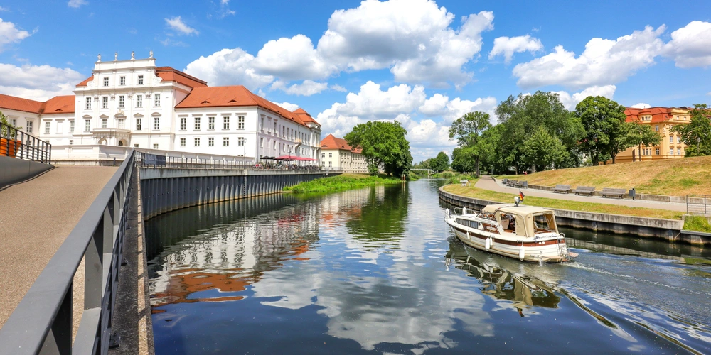 Oranienburg Schloss und Havel Blick auf ein verlassenes Schloss am Fluss, Boot fährt vorbei, blauer Himmel mit Wolken.