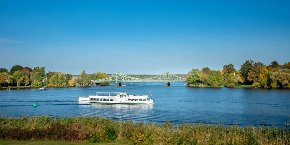 Ein Ausflugsboot fährt auf einem ruhigen Fluss bei klarem, blauem Himmel.