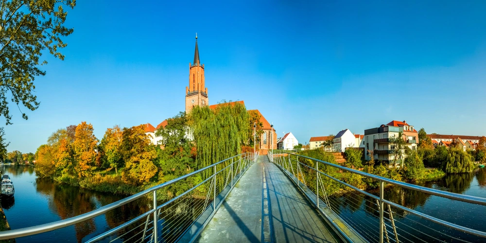 Blick auf eine Brücke mit Aussicht auf eine Kirche und herbstliche Bäume am Fluss.
