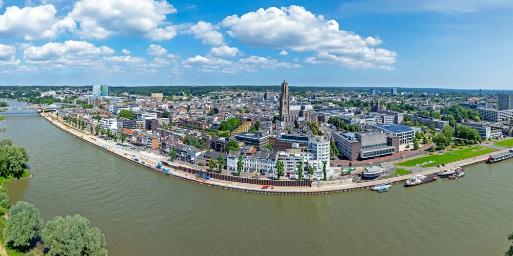 Luftaufnahme einer Stadt am Fluss, mit Wolken und grünen Uferbereichen.