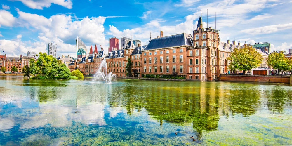 Historisches Gebäude am Wasser, umgeben von Bäumen und reflektiert im See.