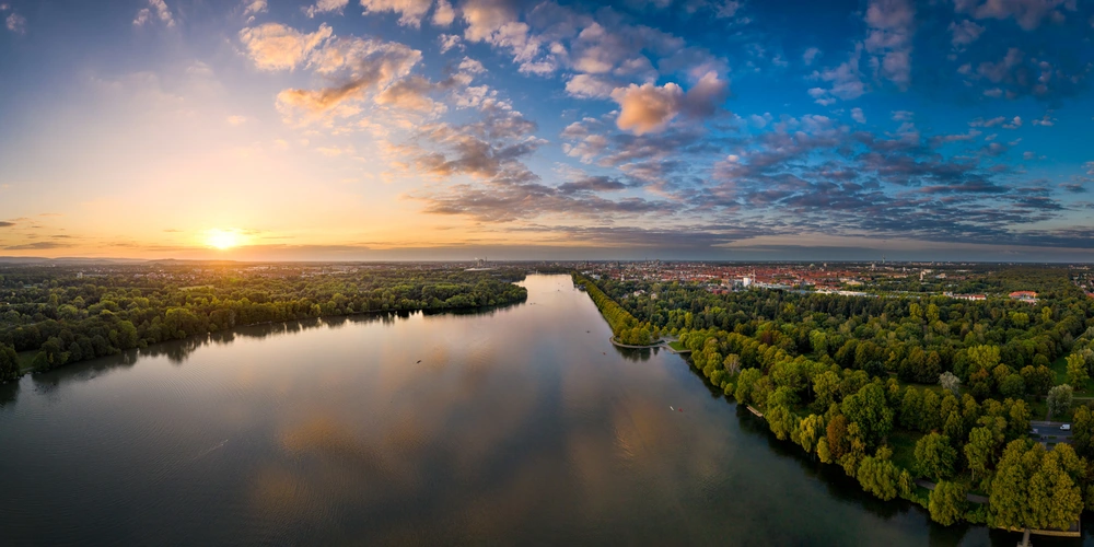 Sonnenaufgang über einem ruhigen Fluss, umgeben von üppigem Grün und wolkenlosem Himmel.