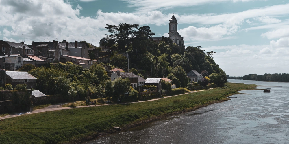 Malerische Landschaft mit einem Fluss, umgeben von Häusern und einem historischen Turm.