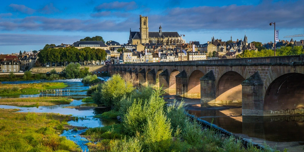 Historische Brücke über einen Fluss mit Stadtansicht im Hintergrund und klarem Himmel.