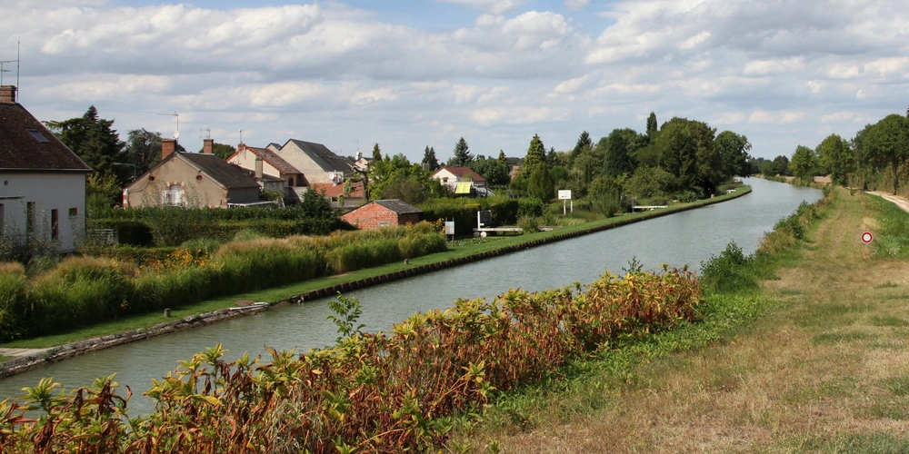 Blick auf einen ruhigen Kanal, umgeben von Häusern und grünen Uferpflanzen.