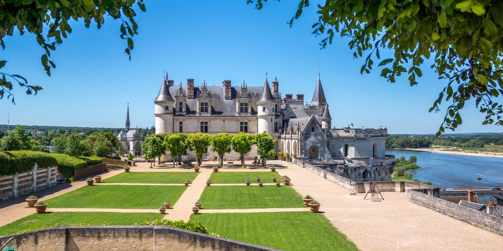 Schloss mit schönen Gärten und Blick auf einen Fluss unter klarem Himmel.
