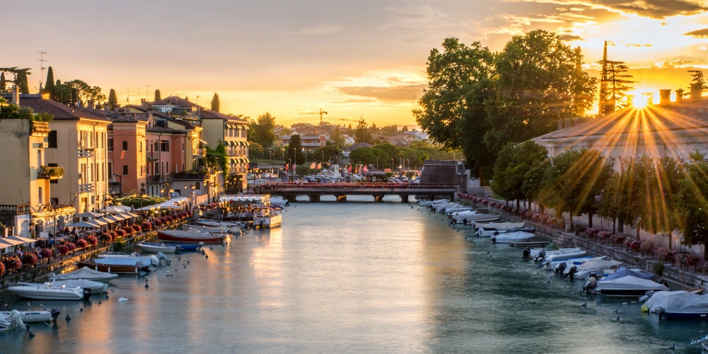 Blick auf einen ruhigen Kanal mit Booten, umgeben von bunten Gebäuden und Sonnenuntergang.