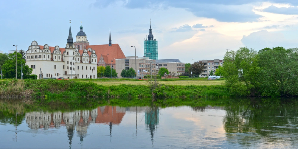Dessau mit Blick über die Mulde  Historische Gebäude mit Türmen spiegeln sich im ruhigen Wasser eines Flusses.