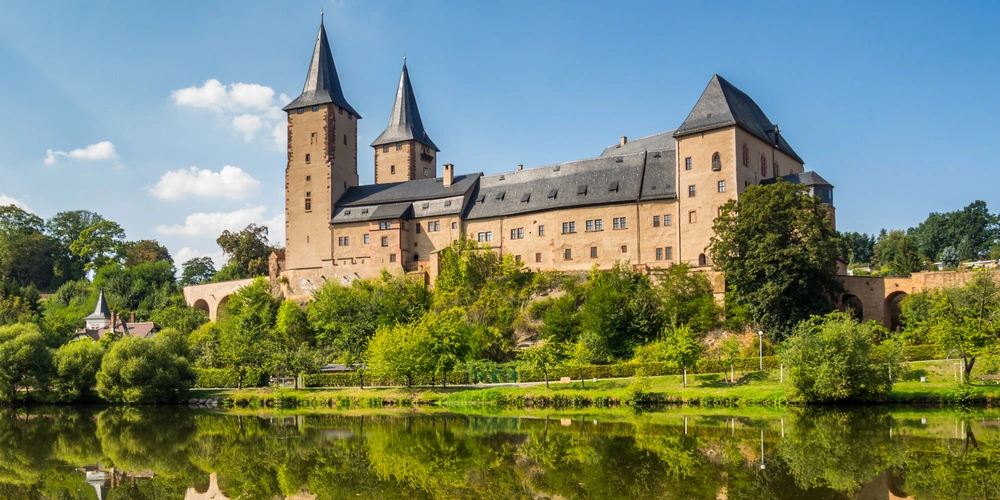 Schloss Rochlitz Eine beeindruckende Burg mit Türmen, umgeben von grünem Landschaft und einem Gewässer.
