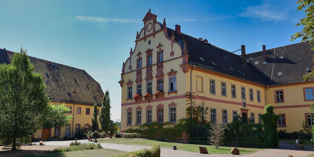 Rittergut Kössern Historisches Gebäude mit gelber Fassade und verzierter Architektur unter blauem Himmel.