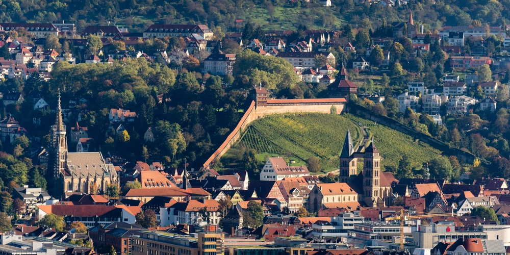Esslinger Altstadt Blick auf die Stadt mit einer Stadtmauer und grünen Hügeln im Hintergrund.