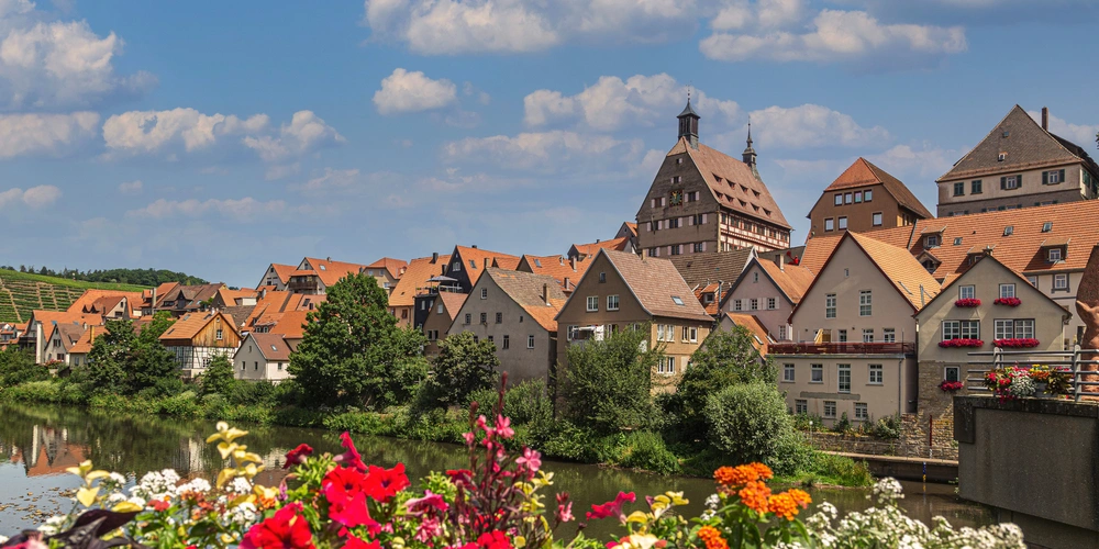 Idyllisches Dorf mit traditionellen Häusern, bunten Blumen und Wolken am Himmel.