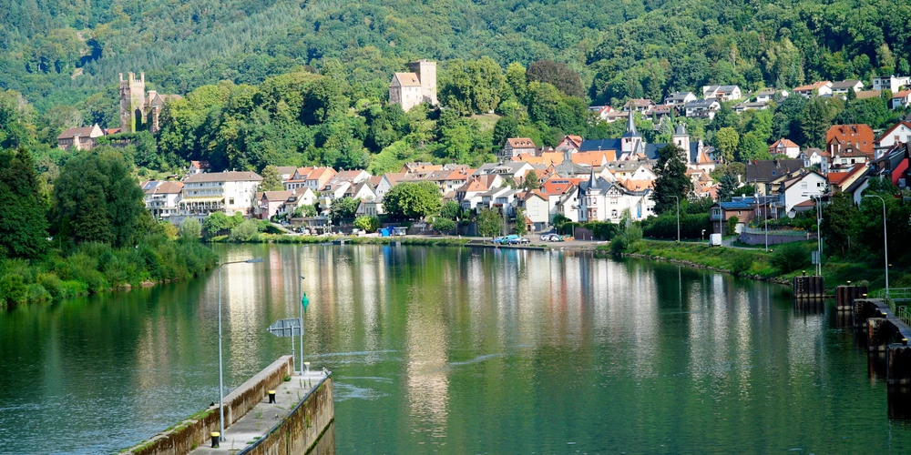 Neckarsteinach Malerische Flusslandschaft mit einer Stadt und grünen Hügeln im Hintergrund.