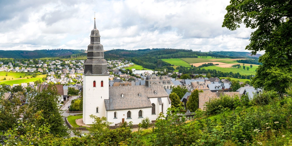 Kirche in Eversberg bei Meschede im Sauerland Weißes Kirchturmgebäude mit Spitze umgeben von grünen Feldern und Hügeln.