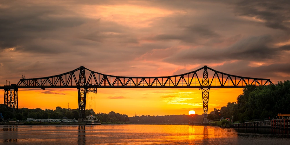 Rendsburger Eisenbahnhochbrücke Stahlbrücke im Sonnenuntergang, reflektiert im ruhigen Wasser.