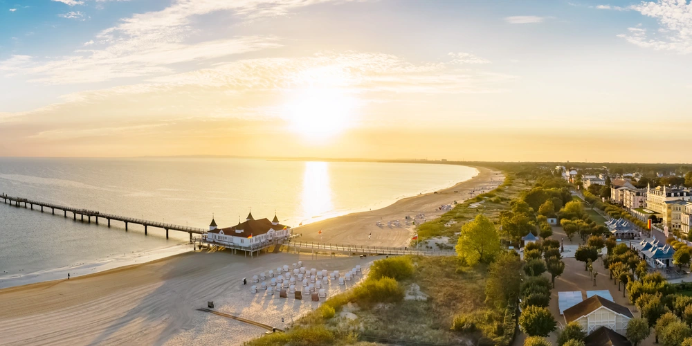 Sonnenuntergang über einem Strand mit Steg und Küstenhäusern.