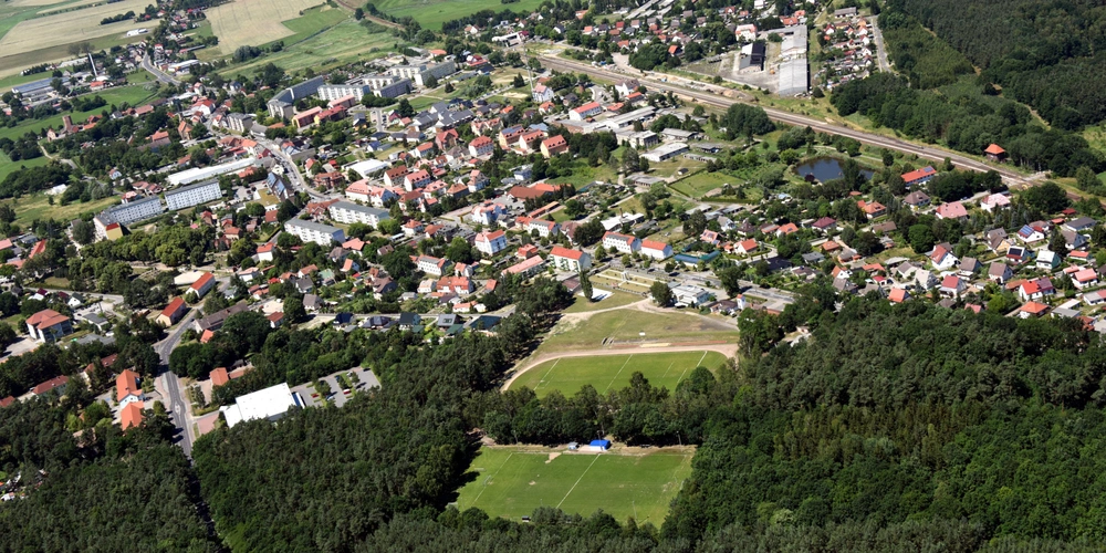 Luftaufnahme einer Stadt mit Wohngebieten, Wäldern und Sportfeldern.