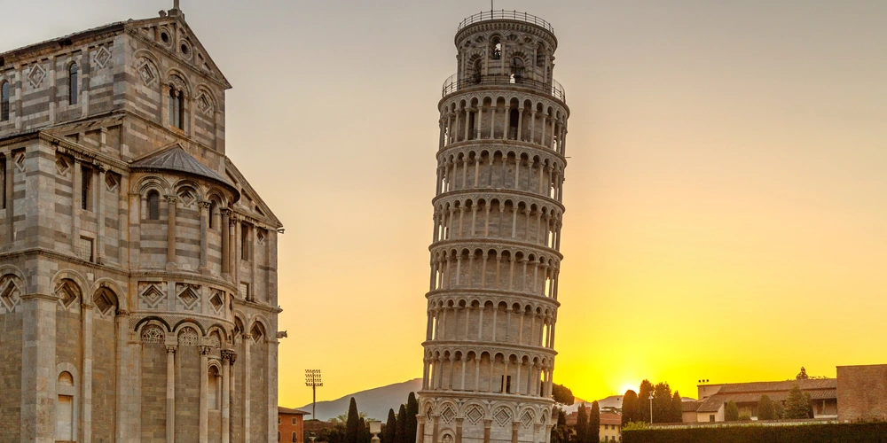 Der schiefe Turm von Pisa vor einem Sonnenuntergang, neben einer historischen Kirche.