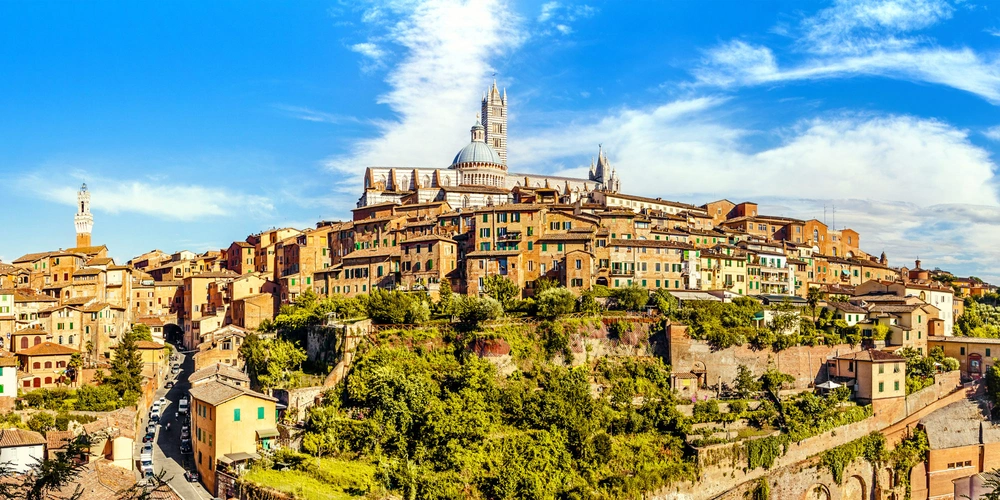 Die Stadt Siena auf einem Hügel, umgeben von grünen Landschaften und blauem Himmel.
